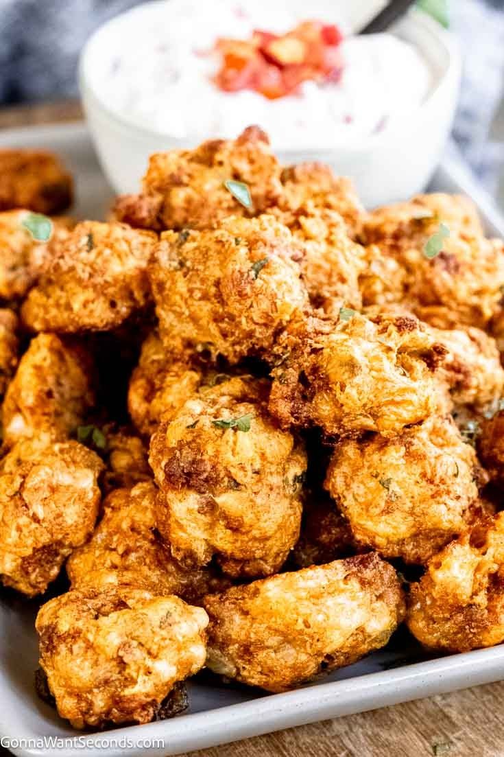 some fried food on a white plate with a bowl of yogurt in the background