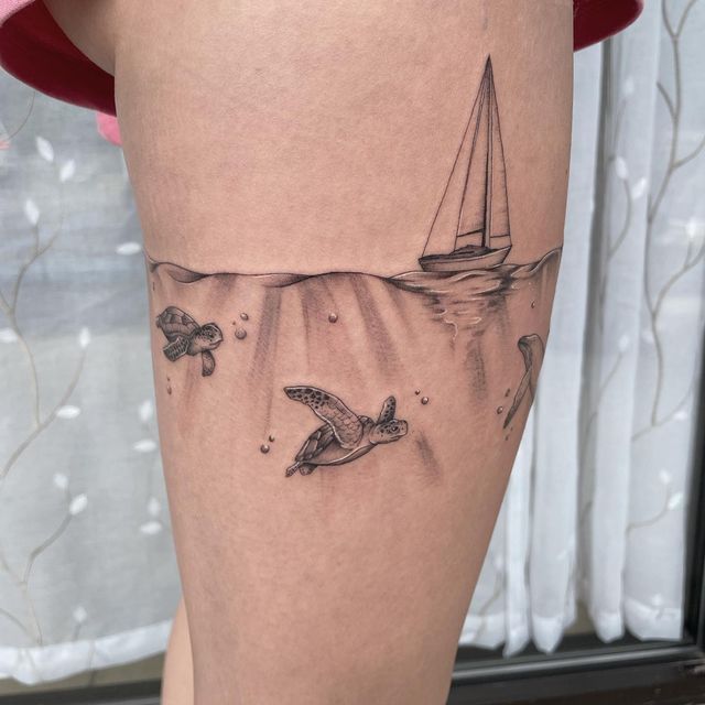 a woman's thigh with a tattoo of a boat and sea turtle on it