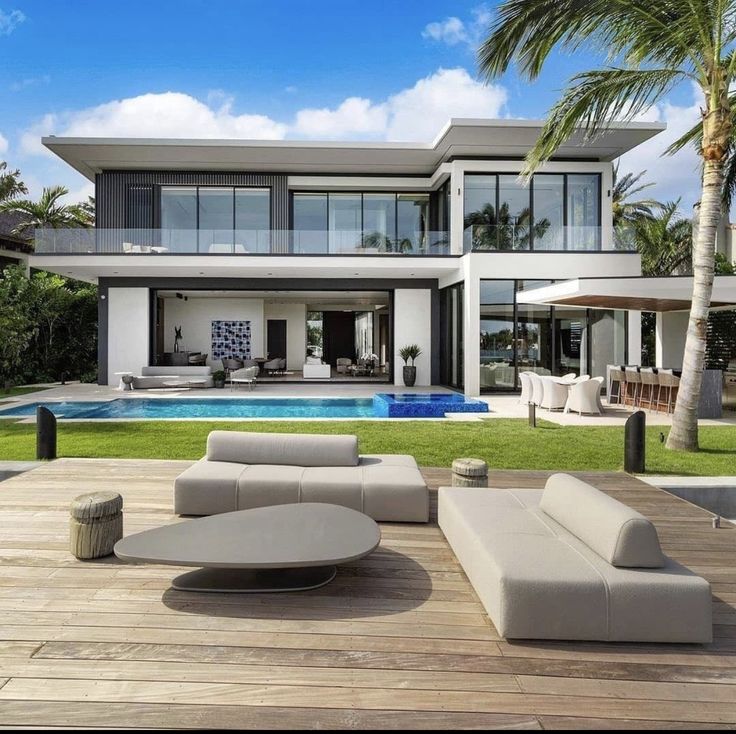 an outdoor living area with couches and tables next to a swimming pool in front of a large house