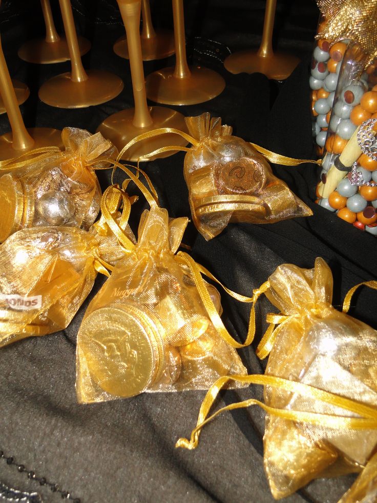 several gold bags with ribbons tied around them on a black table cloth next to other decorations