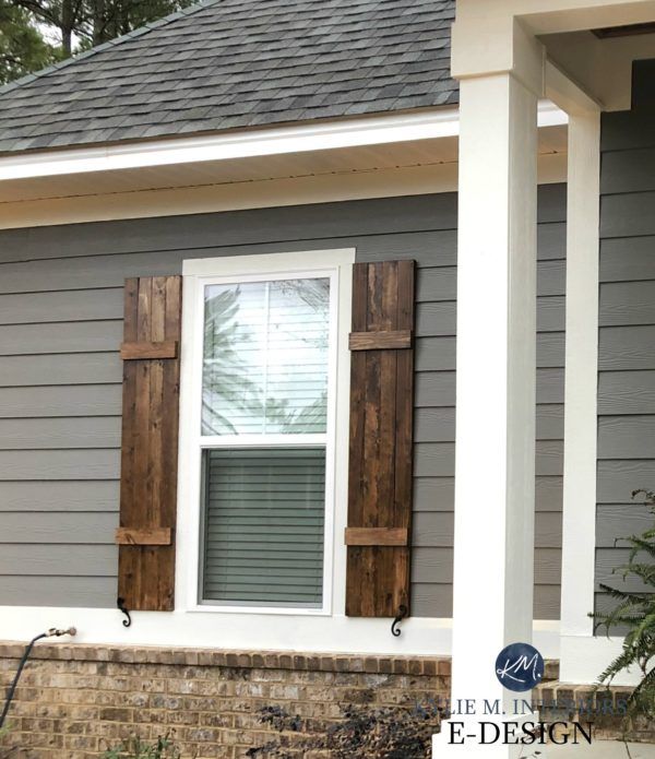 a gray house with shutters on the front and side windows that have wooden shutters