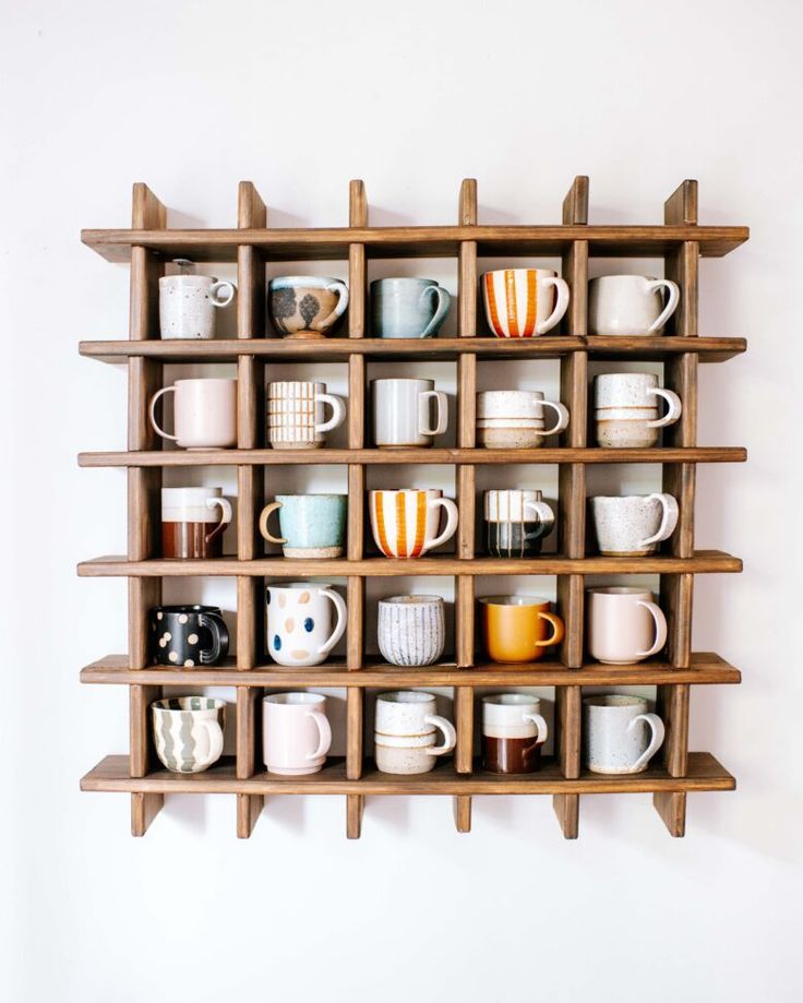 a wooden shelf filled with cups and mugs on top of eachother in front of a white wall