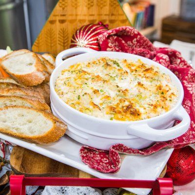 a white bowl filled with cheese and bread on top of a wooden cutting board next to other food