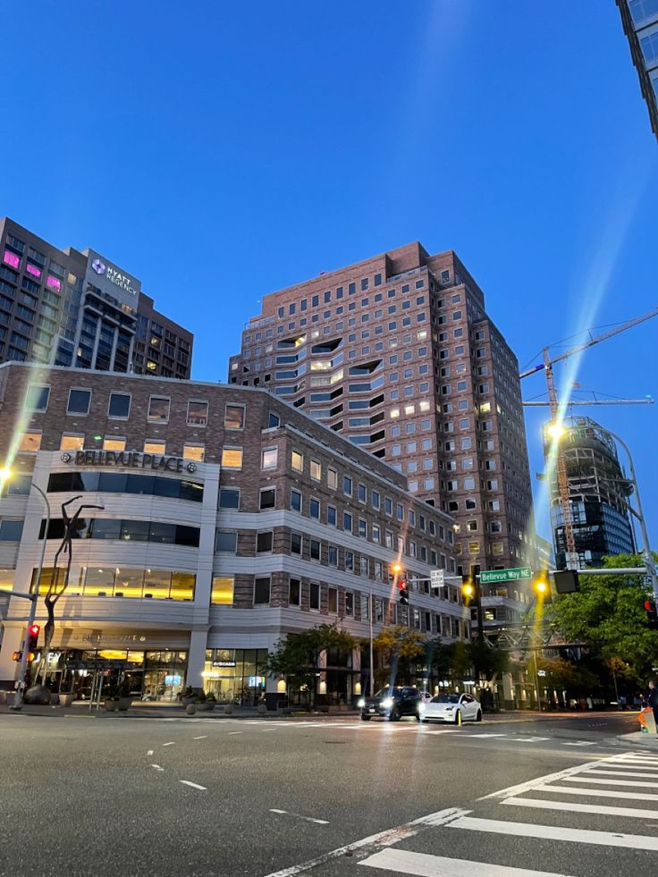 an intersection with traffic lights and tall buildings in the background at dusk, as seen from across the street