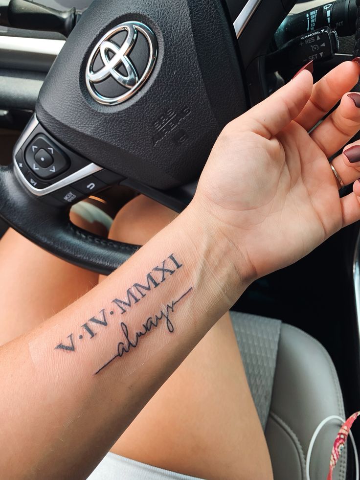 a woman holding the steering wheel of her car with a tattoo on her arm that reads, viv mamma always