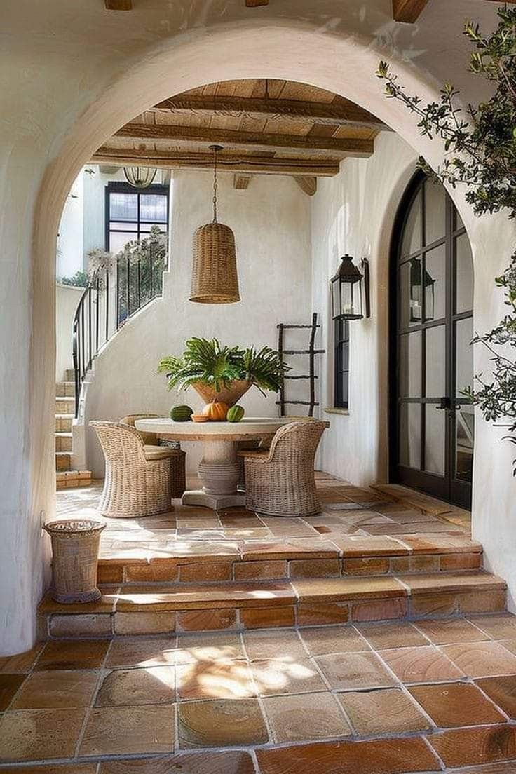 an archway leading to a patio area with potted plants and wicker furniture on the steps