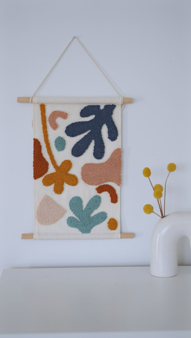 a white vase with yellow flowers and a wall hanging