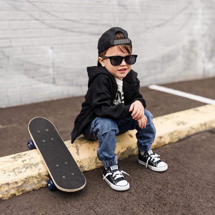 a young boy sitting on top of a skateboard next to a wooden pole and wearing sunglasses