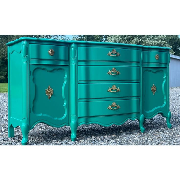 a green dresser with gold handles and drawers on it's sides, sitting in gravel