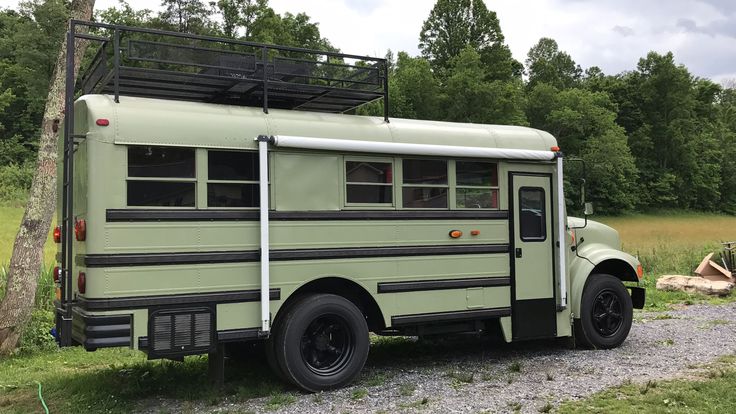 an old green school bus parked on the side of a dirt road next to a tree