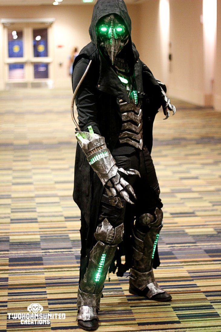 a man dressed up as an alien with green eyes and gloves standing in a hallway