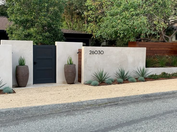 two large planters sitting next to each other on the side of a road in front of a house