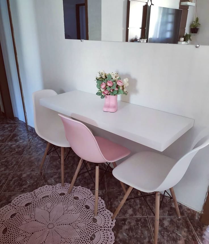 a white table with four chairs and a pink vase on top of it in front of a mirror