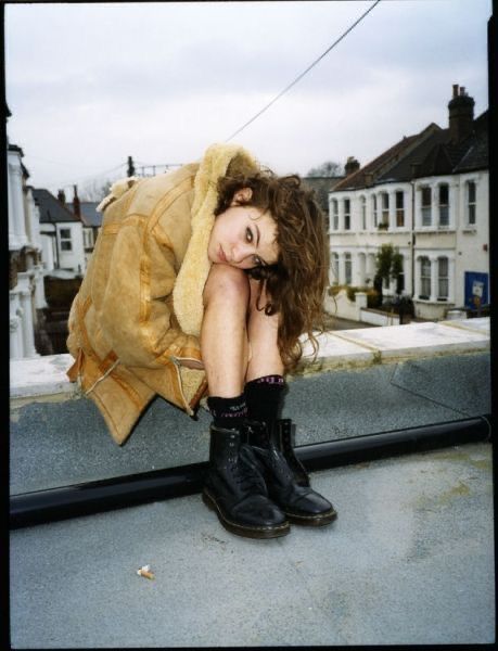 a young woman sitting on top of a roof next to a yellow jacket and black boots