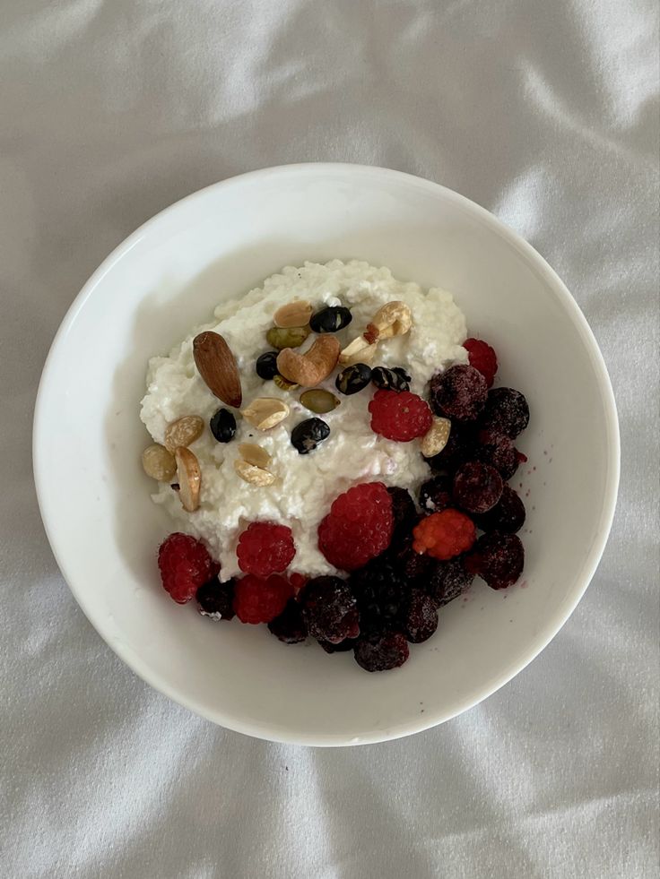 a white bowl filled with oatmeal, berries and nuts