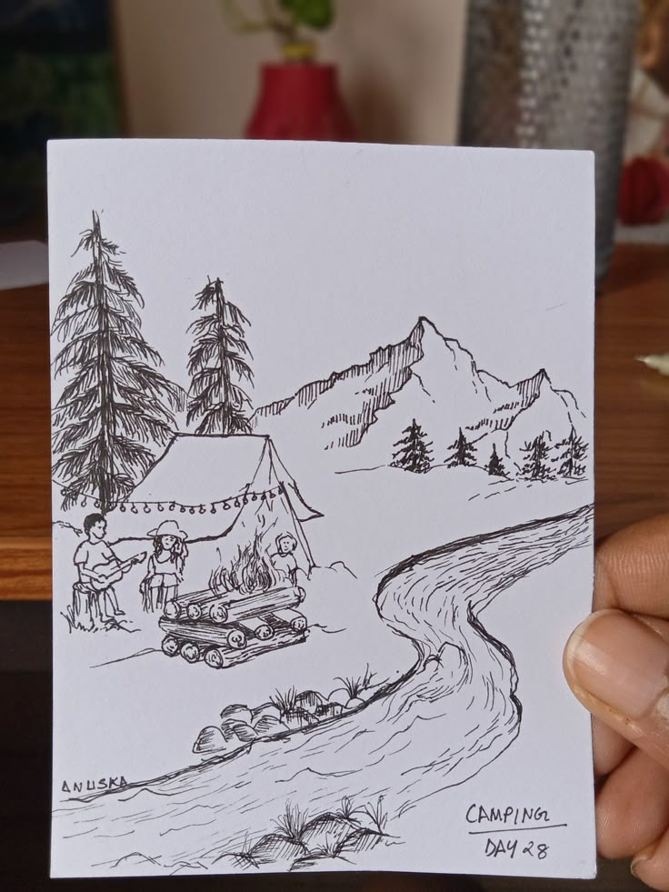 a hand holding up a drawing of a camp site