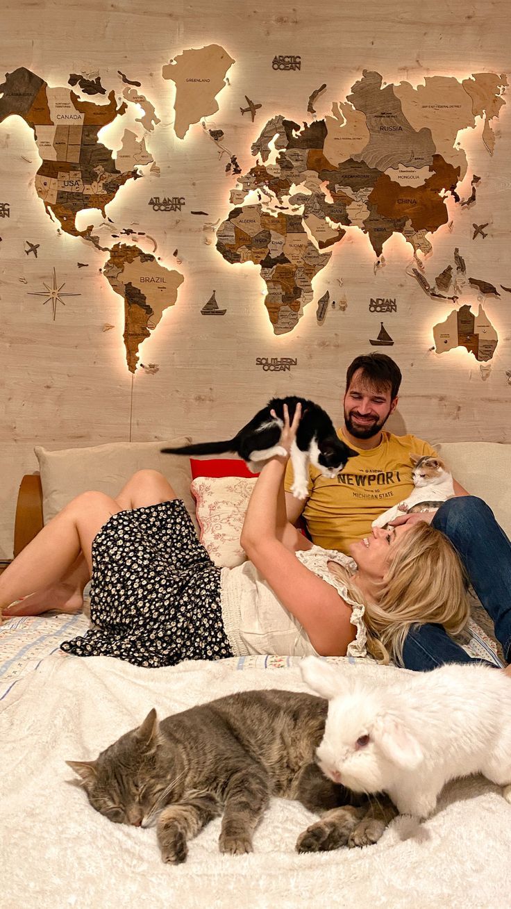 a man and woman laying on a bed with two cats in front of a world map