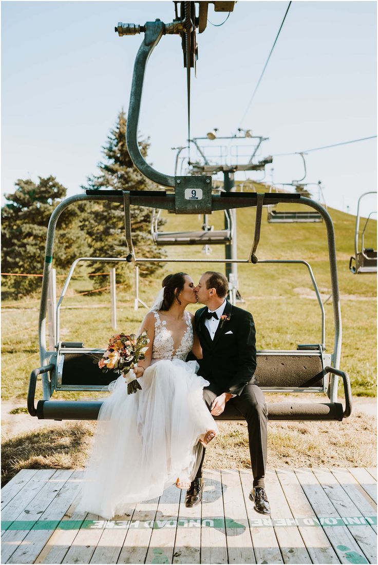 a bride and groom sitting on a bench in front of a ski lift