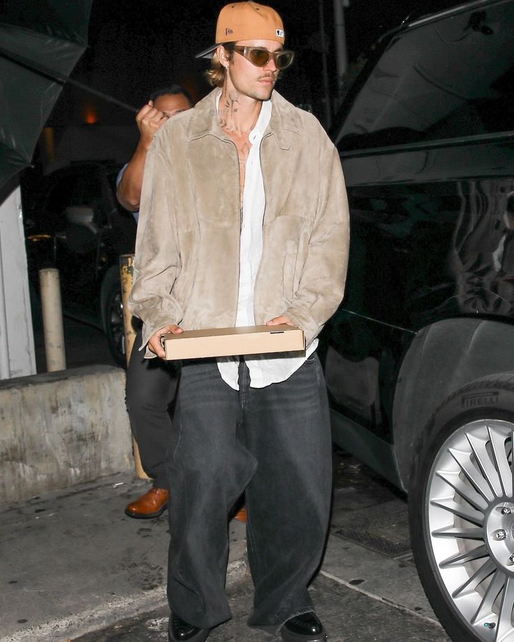 a man carrying a pizza box in his hand while standing next to a black car