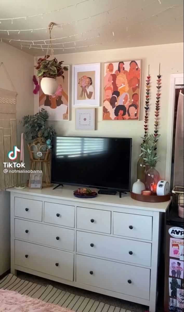 a flat screen tv sitting on top of a white dresser next to a wall filled with pictures