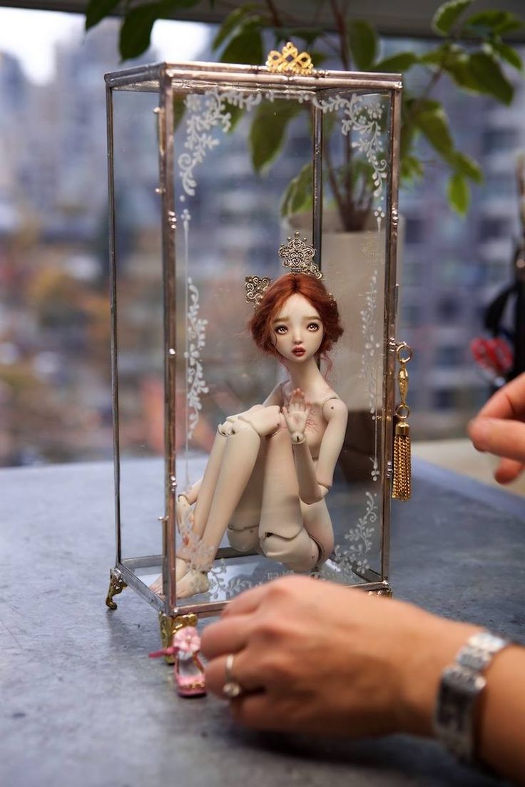 a doll is sitting in a glass box with pearls on it's legs and hands