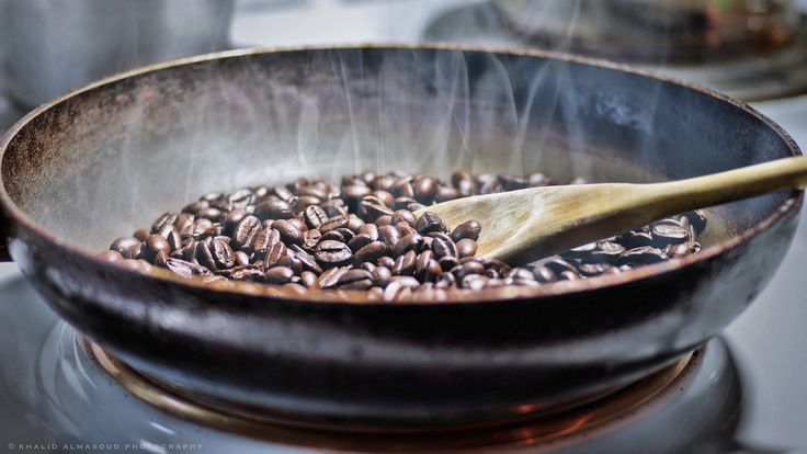 a wooden spoon stirring coffee beans in a skillet