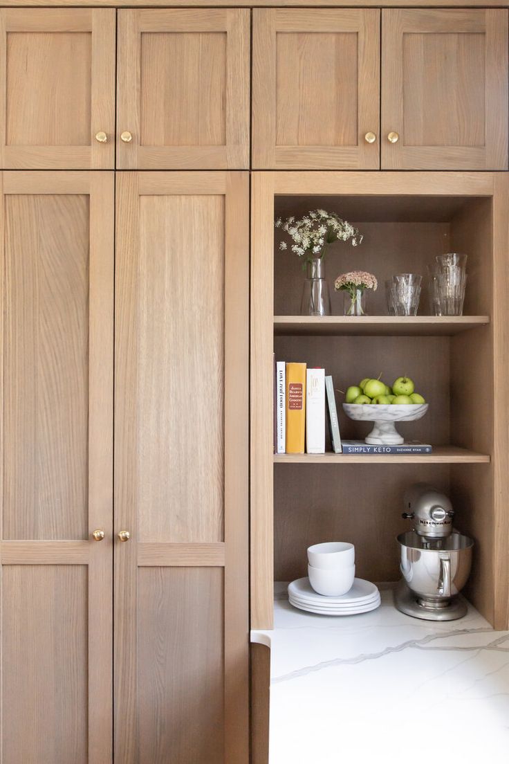 a kitchen with wooden cabinets and white counter tops, along with bookshelves that have glass vases on them