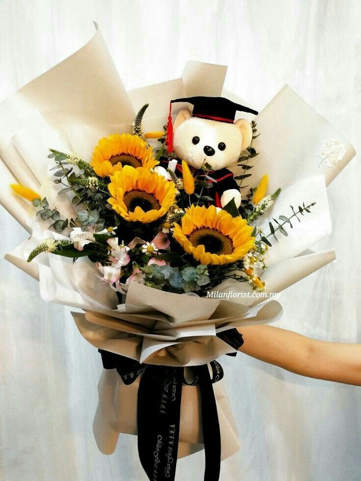 a bouquet of sunflowers with a teddy bear in the middle is held by someone's hand