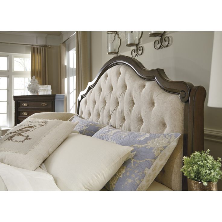 a bed with pillows on top of it in front of a dresser and window sill