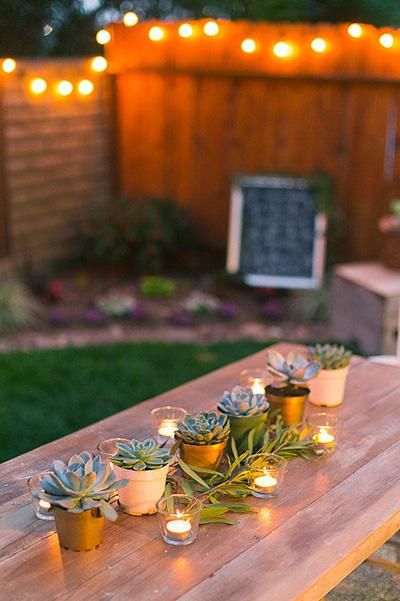 a wooden table with candles and succulents on it in front of a fence