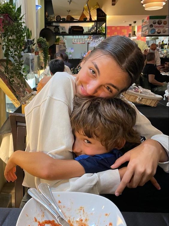 a woman hugging a boy while he is eating food from a bowl on the table