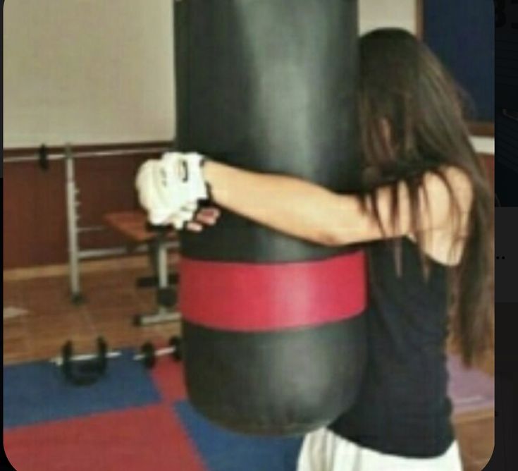 a woman is standing next to a punching bag in a room with red and black mats