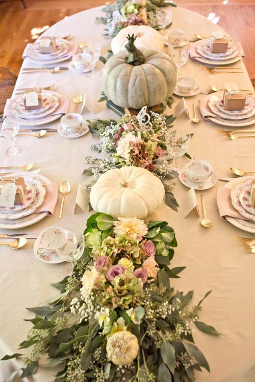 the table is set with white pumpkins and greenery on it, along with other place settings