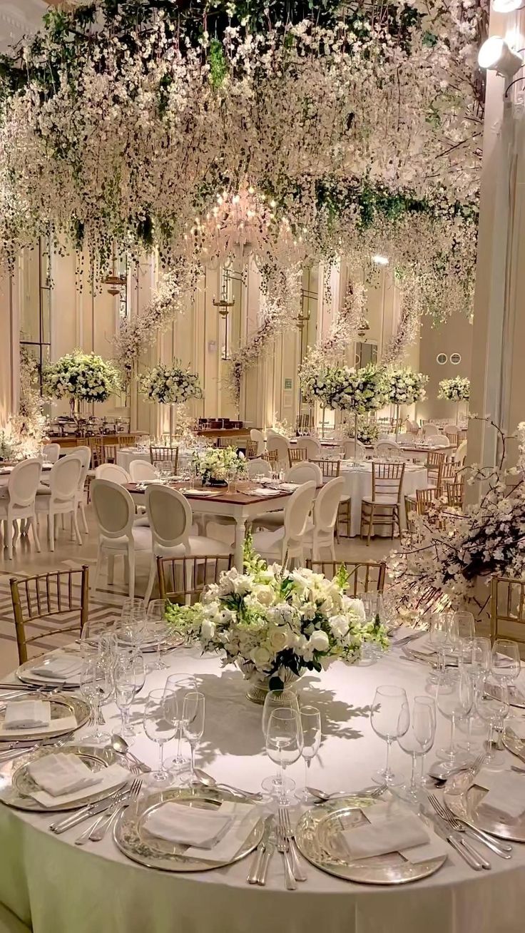 the tables are set up with white flowers and place settings for an elegant wedding reception