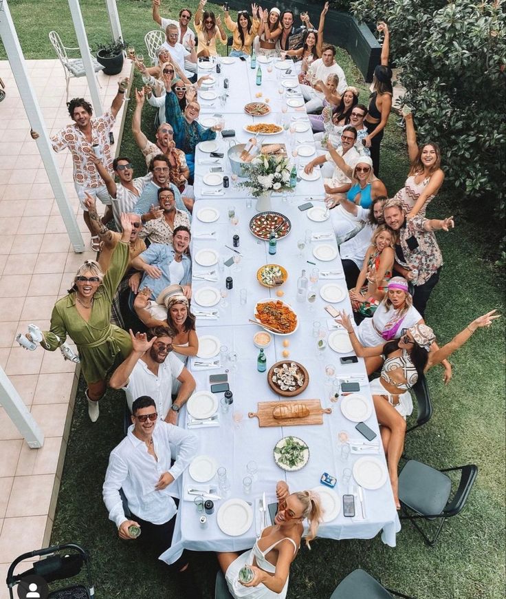 a group of people sitting at a long table with plates and bowls on it, posing for the camera