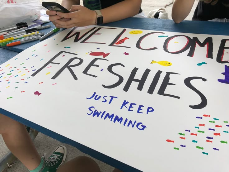 two people sitting at a table with a sign that says welcome freshies just keep swimming