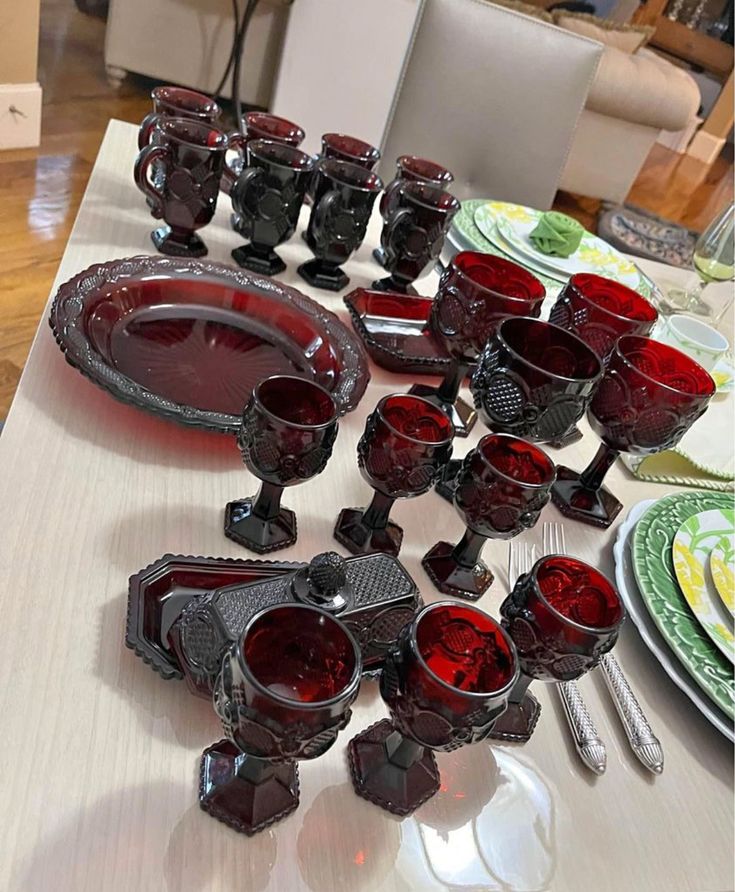 the table is set with red glass dishes and silverware