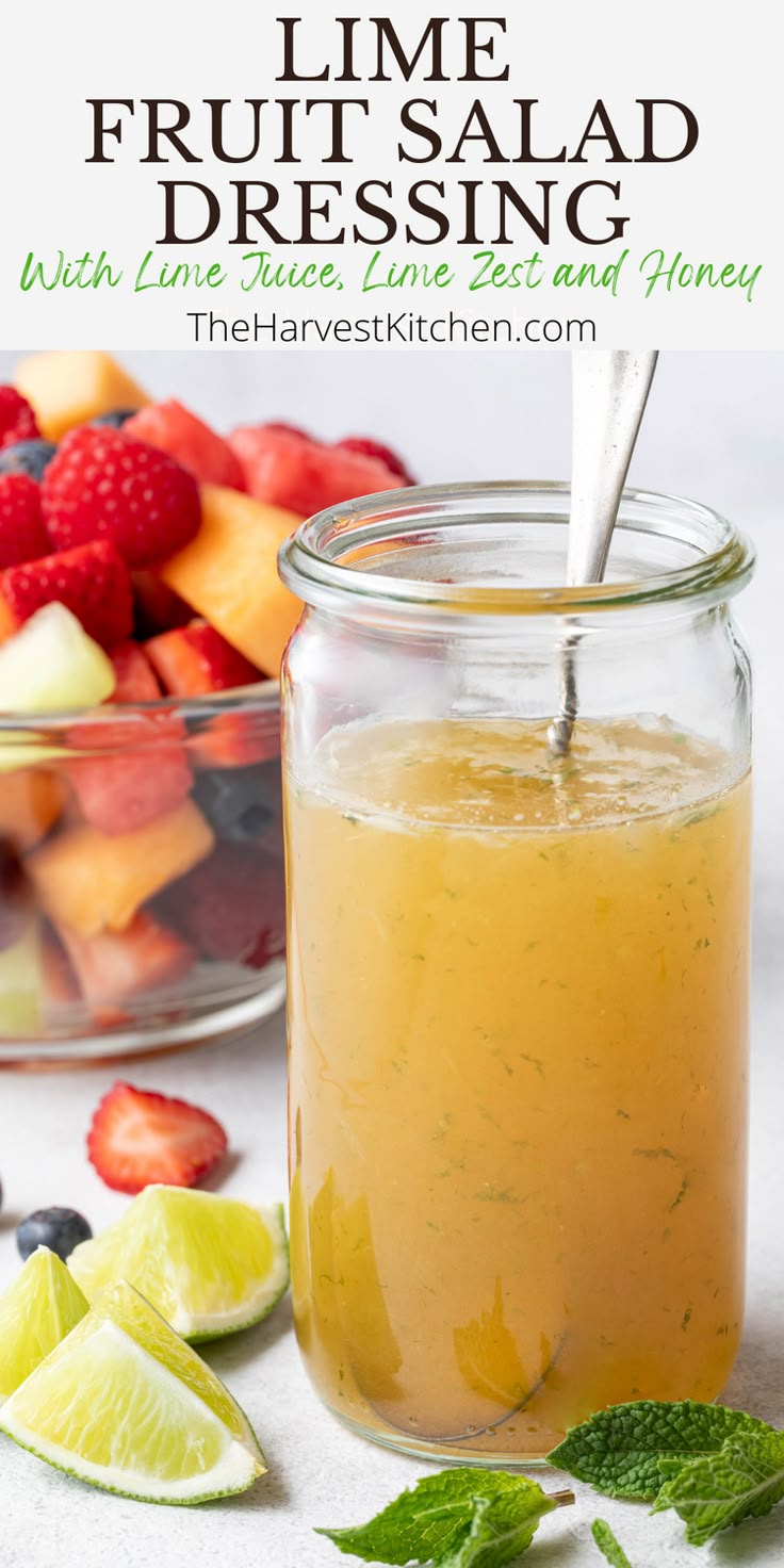 a glass jar filled with fruit salad dressing next to sliced strawberries and limes