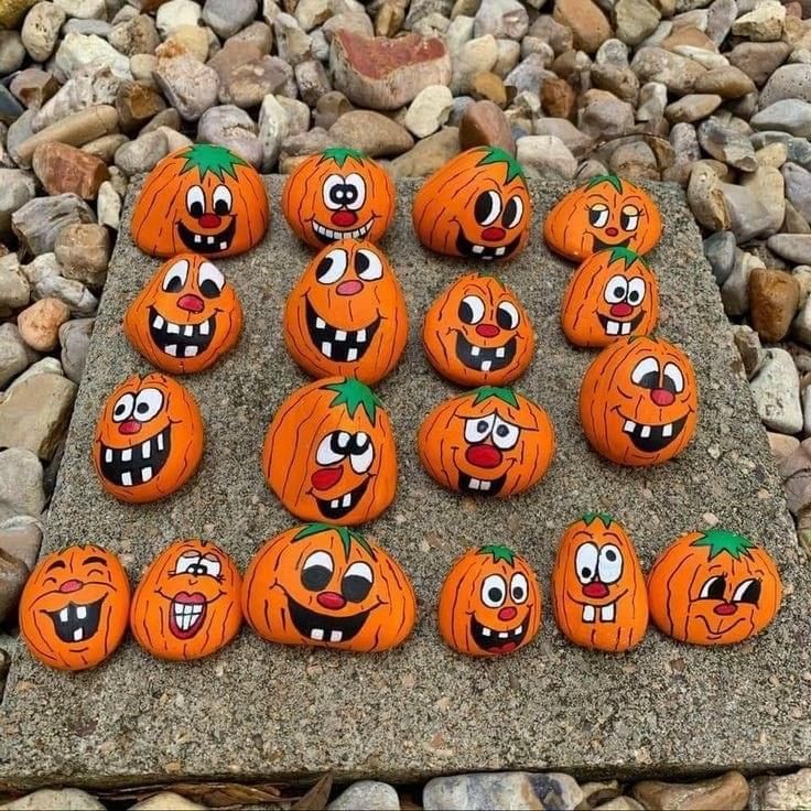 there are many pumpkins with faces painted on them sitting on the ground next to some rocks