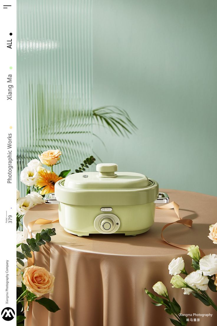 a green crock pot sitting on top of a table next to white and yellow flowers