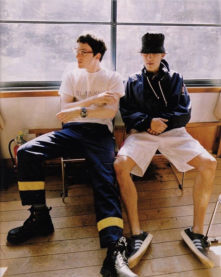 two young men sitting next to each other in front of a window, one holding a baseball bat