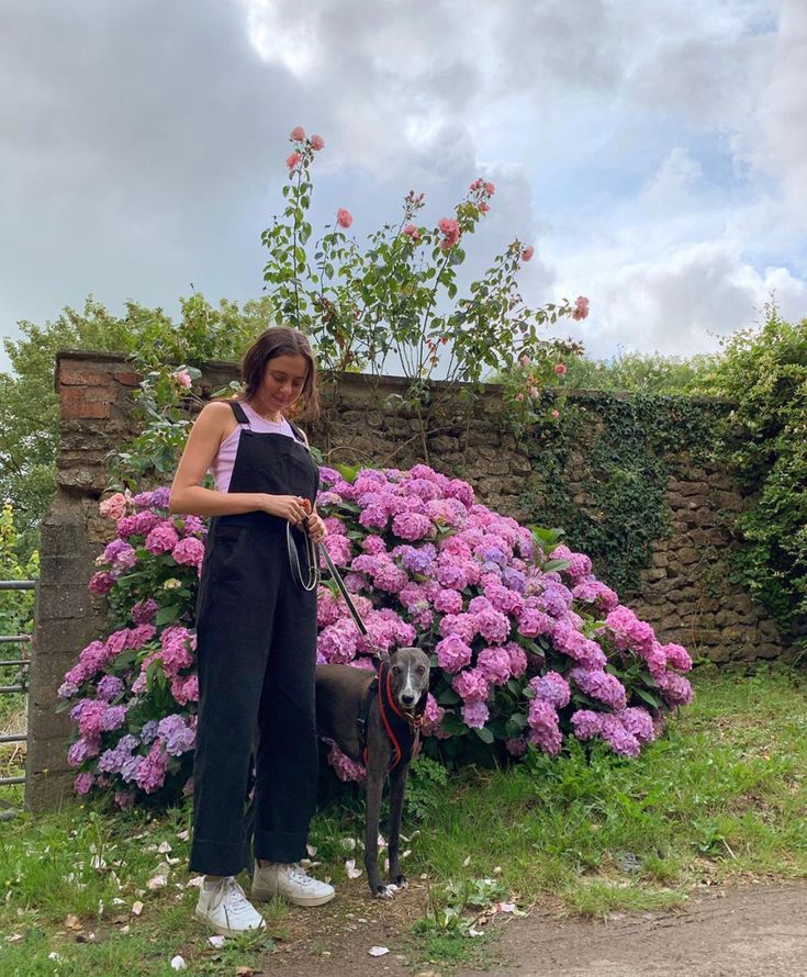 a woman standing next to a dog in front of flowers