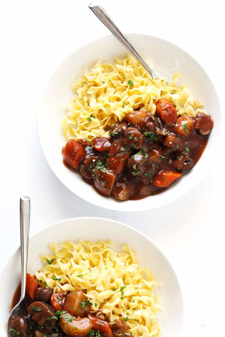 two white bowls filled with pasta and meat covered in tomato sauce on top of a white table