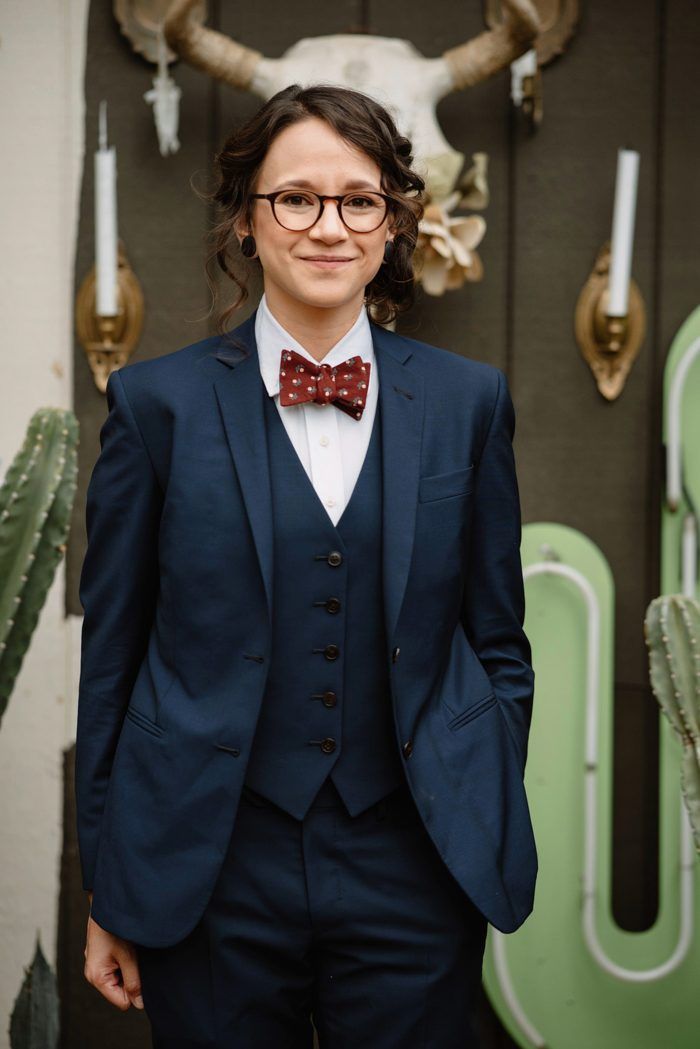 a woman in a suit and bow tie standing next to cactuses with horns on the wall behind her