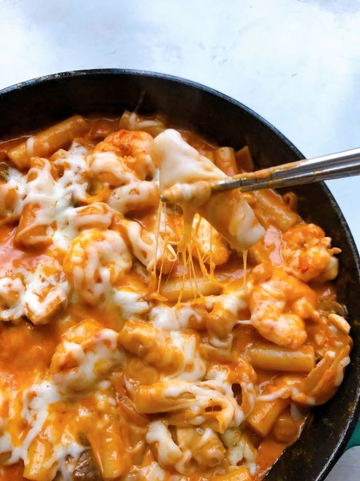 a skillet filled with pasta and cheese on top of a table next to a fork