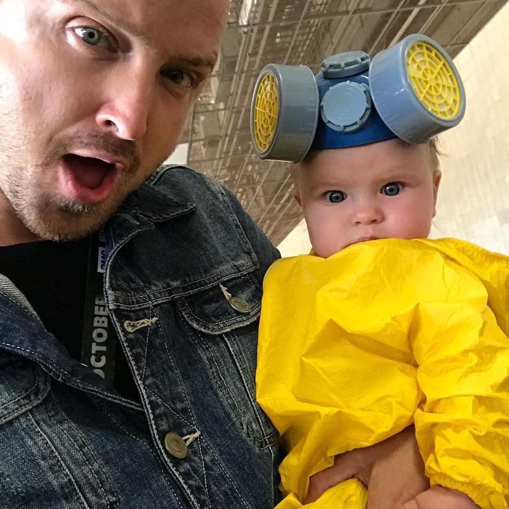 a man holding a baby wearing a yellow raincoat and goggles on his head