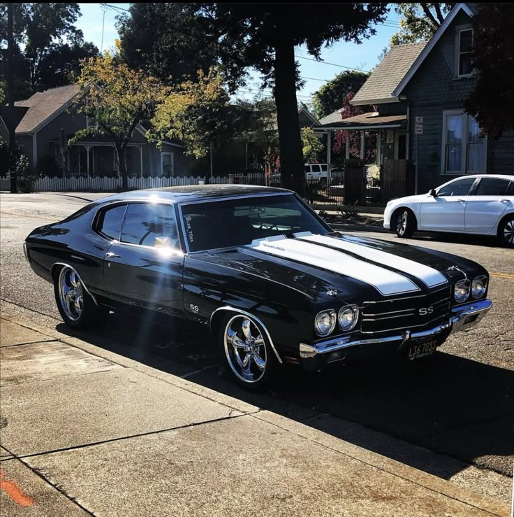 a black and white muscle car parked on the side of the road in front of some houses