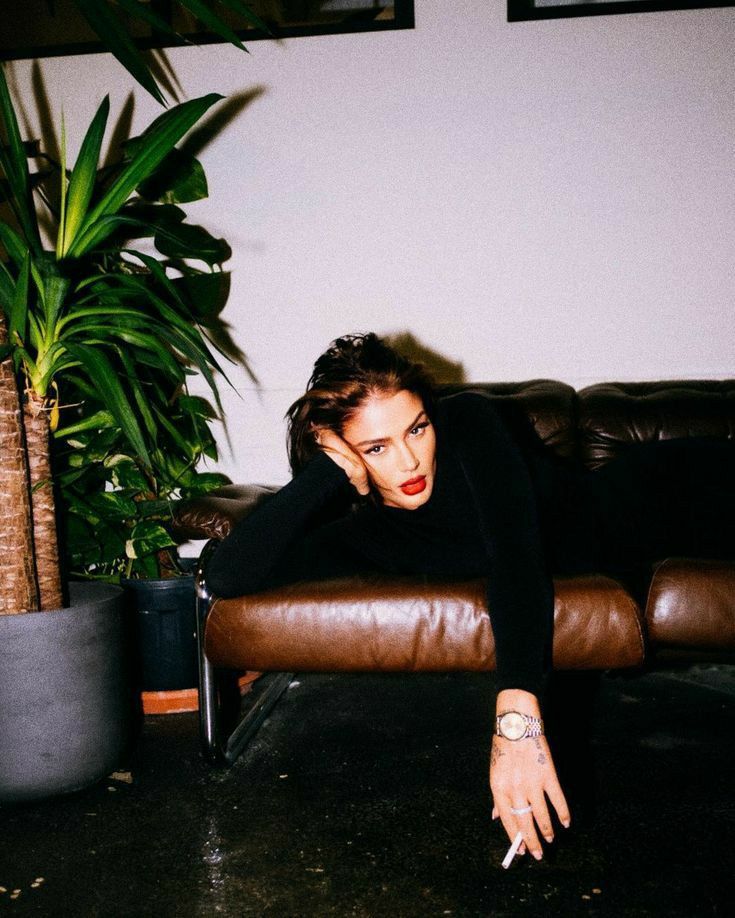 a woman sitting on top of a brown couch next to a potted plant