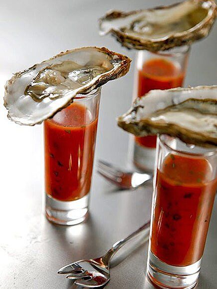 three glasses filled with oysters on top of a table next to silver utensils