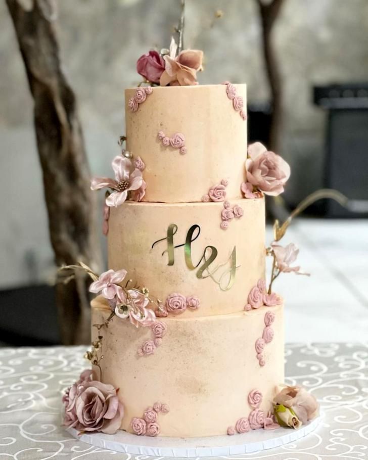 a three tiered wedding cake with pink flowers on the top and initials on the bottom